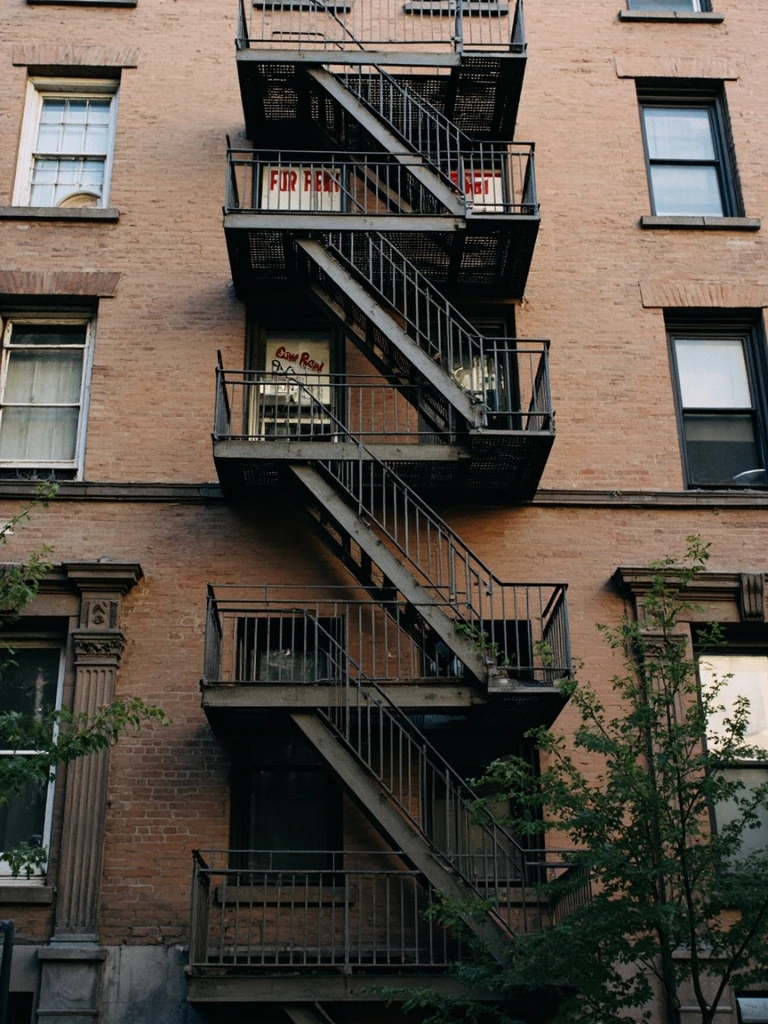 A walk-up apartment building in Brooklyn with weathered fire escapes and faded rental signs.