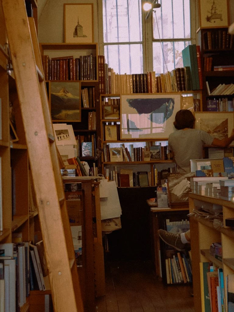 A small independent bookstore window glowing onto the sidewalk at dusk.